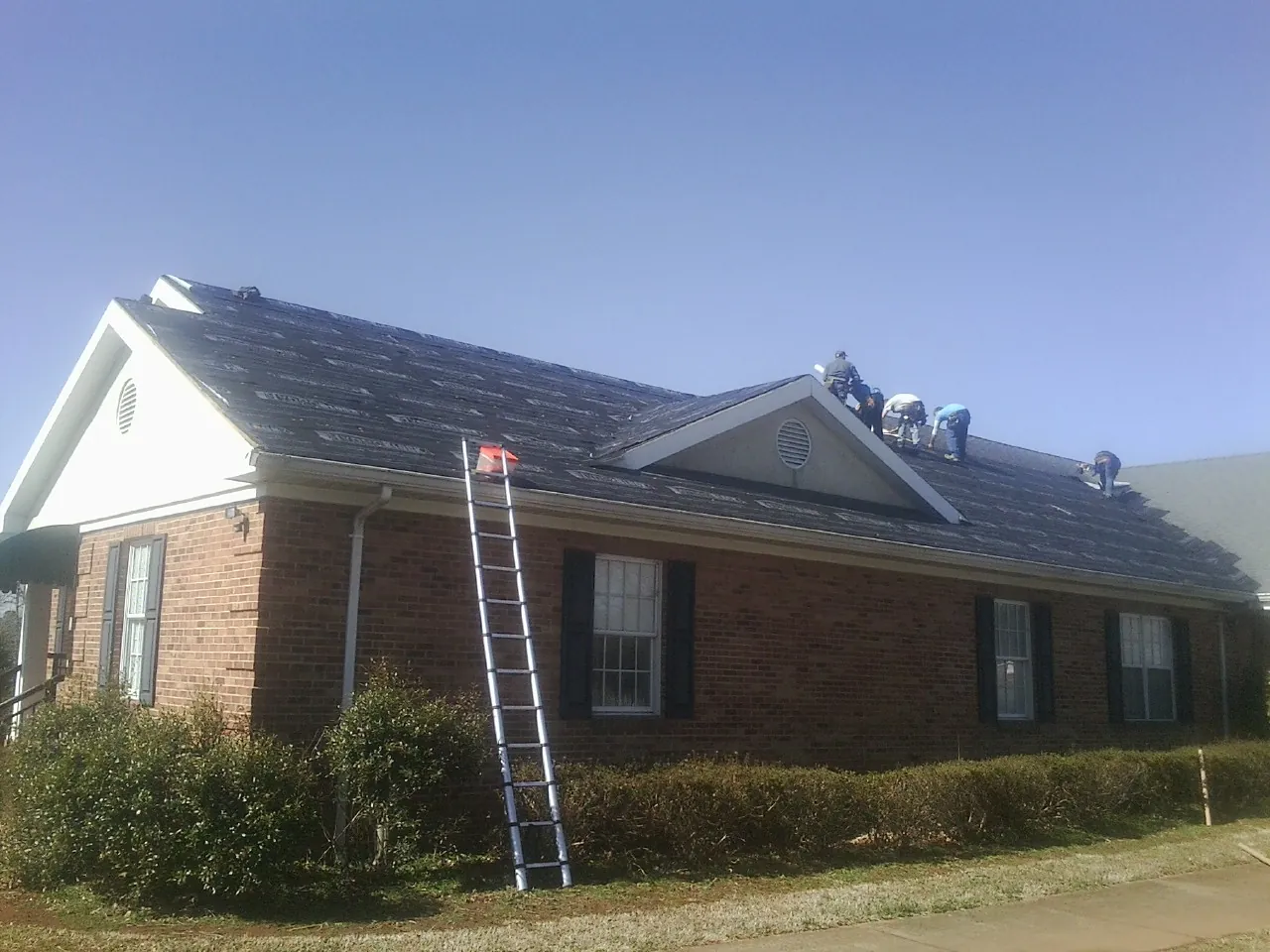 Crew tearing shingles off a brick ranch roof with a ladder set — Emergency Roof Repair work by our crew in Forney