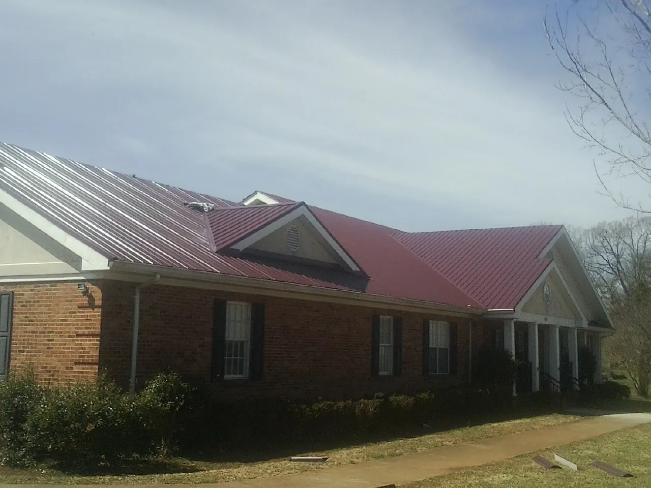 Red metal roof with gabled entries on a long brick building, from a Hail Damage Roof Repair job in Forney