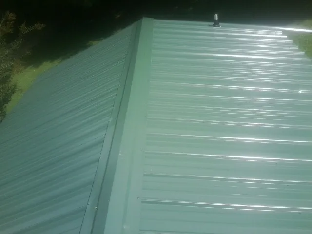 New green metal panels meeting at the ridge of a roof — Flat Roof Repair work by our crew in Forney