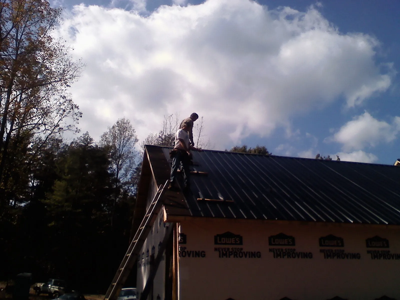 Roofer fastening dark metal panels high against a cloudy sky, from a Roof Inspection job in Forney